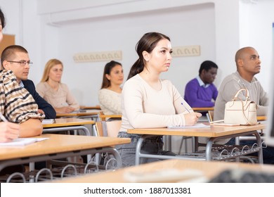 Focused Young Attractive Brunette Listening To Lecture In Classroom With Group Of Adult People. Postgraduate Education Concept