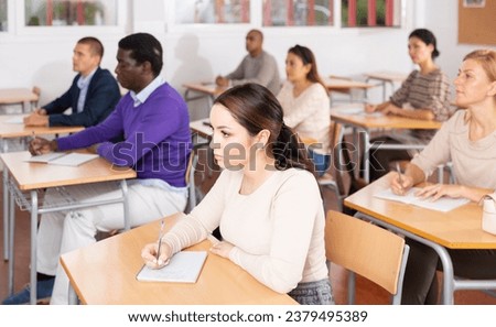 Focused young attractive brunette listening to lecture in classroom with group of adult people. Postgraduate education concept