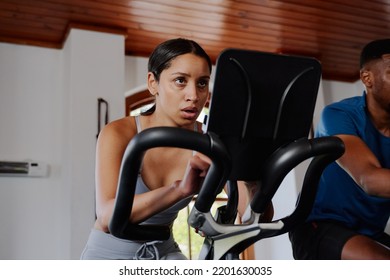 Focused Young Biracial Woman And Black Man Using Exercise Bike At The Gym