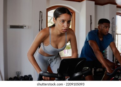 Focused Young Biracial Woman And Black Man Doing Cardio Exercise Bike At The Gym