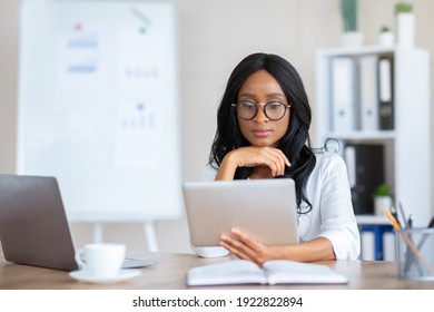 Focused Young Black Business Lady Using Tablet Pc At Her Workplace In Modern Office. Confident Millennial Entrepreneur Reading Important Document Online, Checking Email, Having Business Conference