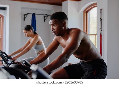 Focused Young Black Man And Biracial Woman Using Exercise Bike At The Gym