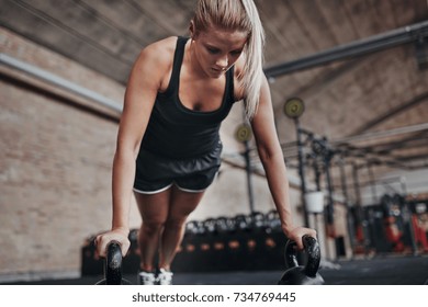 Focused young blonde woman in exercise clothing working out alone with weights on a gym floor - Shutterstock ID 734769445