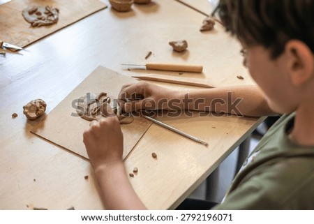 Focused young boy sitting at a workshop table and shaping a clay portrait, representing creative activity, artistic expression, and child development.