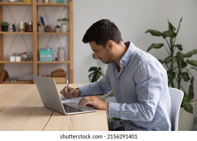 Focused Young Business Professional Man Using Laptop Computer At Home, Analyzing Marketing Report. Student Studying At Home, Using Learning App, Writing Notes At Table