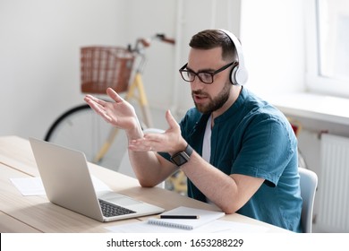 Focused young businessman in eyewear wearing headphones, holding video call with clients on laptop. Concentrated millennial man in glasses giving online educational class lecture, consulting customer.