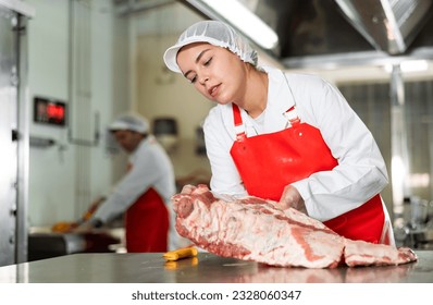 Focused young butcher shop saleswoman cutting fresh raw pork ribs at meat processing table.. - Powered by Shutterstock