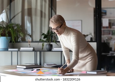 Focused young Caucasian businesswoman in glasses consider work with paper company financial project in office. Serious 30s female employee brainstorm analyze paperwork documentation at workplace.