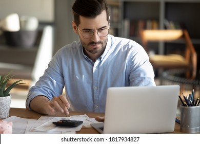 Focused young Caucasian man look at laptop screen calculate expenses expenditures pay bills taxes online. Millennial male busy managing household family budget, take care of financial paperwork.