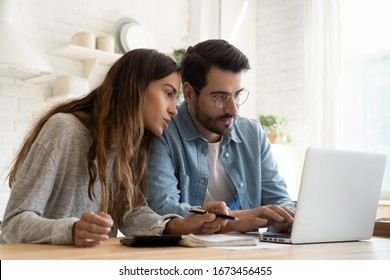 Focused young couple calculating bills  discussing planning budget together  serious wife   husband looking at laptop screen  using online banking services   calculator  checking finances