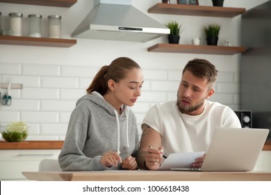 Focused young couple checking analyzing utilities bills sitting together at kitchen table, serious husband and wife reading bank loan documents with laptop, family managing finances planning expenses