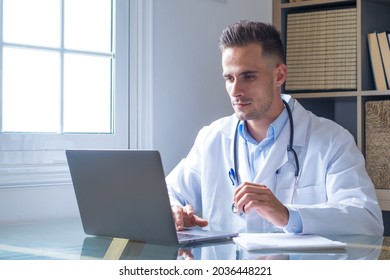 Focused Young Doctor Wearing Glasses Working On Laptop In Office, Sitting At Desk, Looking At Screen, Serious Therapist Gp Writing Report Or Email, Consulting Patient Online, Filling Medical Card