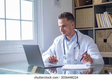 Focused Young Doctor Wearing Glasses Working On Laptop In Office, Sitting At Desk, Looking At Screen, Serious Therapist Gp Writing Report Or Email, Consulting Patient Online, Filling Medical Card