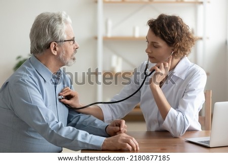 Focused young female cardiologist or general practitioner in white coat listening heartbeat or elderly senior male patient at checkup meeting, preventing cardiovascular disease, healthcare concept.
