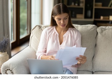 Focused young female homeowner studying paper bills, insurance, mortgage, loan agreement from bank, doing paperwork at home. Student receiving, reading document from school, college at laptop