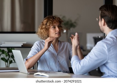 Focused young female manager holding negotiations meeting with serious hispanic male colleague, discussing marketing strategy development or business project ideas together in modern office room.