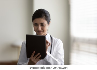 Focused Young Female Practitioner Using Tablet Computer. Indian Doctor Giving Online Virtual Consultation, Chatting To Patient, Making Video Call, Virtual Appointment On App. Telemedicine Concept