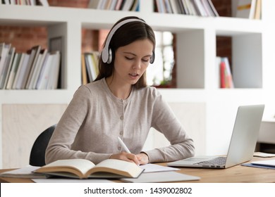 Focused young female student sit at desk wearing headphones listen to music studying, concentrated girl write in notebook make notes prepare home assignment enjoying tracks in earphones - Shutterstock ID 1439002802