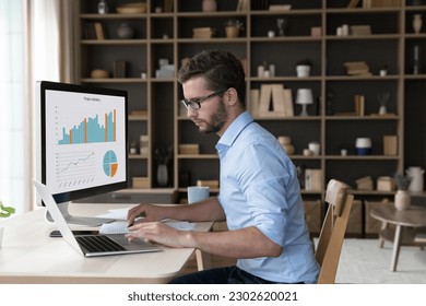 Focused young freelance business man analyzing financial data on desktop large display, working on marketing chart, sales report, using modern Internet technology for job, typing on laptop - Powered by Shutterstock