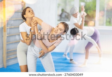 Focused young girl practicing basic protection skills in mock bout with female opponent during self defense course in gym, trying to escape rear grab attack technique, striking chin with elbow