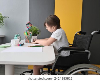 A focused young girl sits in a wheelchair at a white table, diligently drawing with colored pencils in a brightly lit room - Powered by Shutterstock