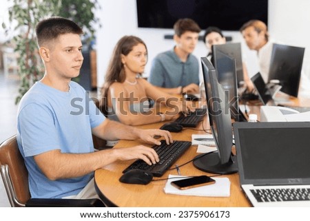 Focused young guy studying in computer lab with fellow students engrossed in coursework..