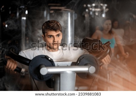 Focused young guy working out in modern gym, pumping up deltoid muscles of shoulders in lateral raise exercise machine. Active lifestyle concept and sports.