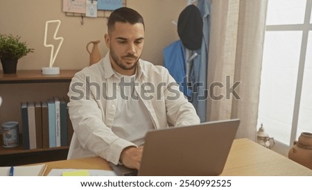 A focused young hispanic man working on a laptop in a modern home office setting