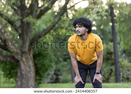 Focused young Indian athlete pausing during workout in park setting, showcasing determination and healthy lifestyle.