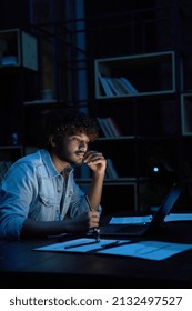 Focused Young Indian Ethnic Business Man, Student Or Web Designer Working On Laptop Computer Late At Night At Home Or In Dark Office Thinking Watching Webinar Learning Online Course Sitting At Desk.