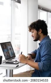 Focused young indian man listening interracial speakers watching lecture seminar webinar online and writing notes looking at laptop screen. Studying remotely or distant interview side view - Shutterstock ID 2083154533