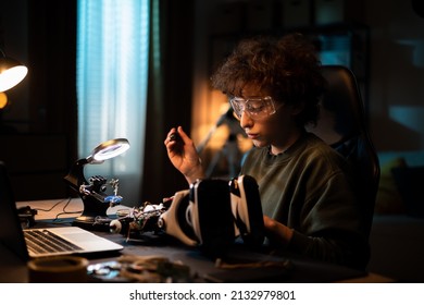 Focused young intelligent boy is passionate about building a robot, doing electronics, connecting wires, soldering cables late at night, child has safety glasses - Powered by Shutterstock