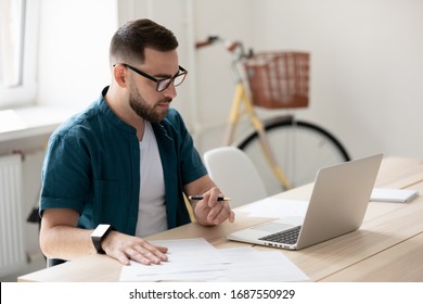 Focused young male employee in glasses watch webinar on laptop make notes, concentrated millennial man worker sit at desk in office study or work on computer, handwrite on paper summarizing - Shutterstock ID 1687550929