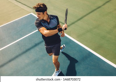 Focused young male tennis player hitting a forehand. Tennis player playing a match on hard court. - Powered by Shutterstock