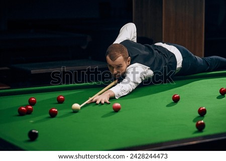 Focused young man lines up his shot on the billiards table, showcasing precision and skill. Promotion of local billiards tournament. Concept of billiards sport, gambling, hobby, leisure, game