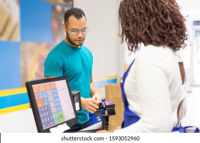 Focused Young Man Paying Bill In Store. Back View Of Cashier Standing At Workplace. Shopping Concept