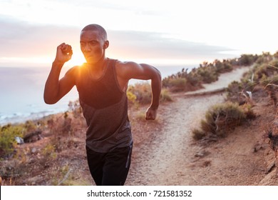 Focused young man running alone along a trail by the ocean while out for a cross country run in the late afternoon - Powered by Shutterstock