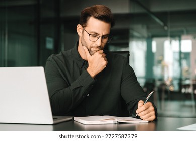 Focused young man student using laptop computer for business studying watching online webinar e-learning training meeting writing notes. European businessman entrepreneur working in office, copy space