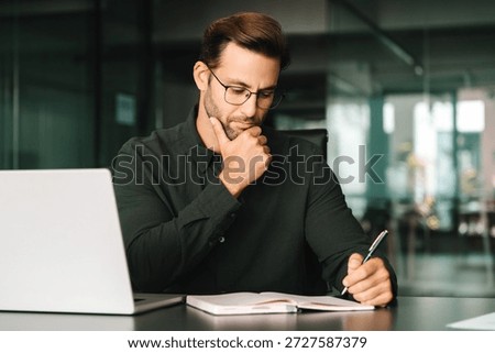 Focused young man student using laptop computer for business studying watching online webinar e-learning training meeting writing notes. European businessman entrepreneur working in office, copy space