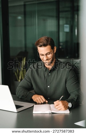 Focused young man student using laptop computer for business studying watching online webinar e-learning training meeting writing notes. European businessman entrepreneur working in office. Vertical