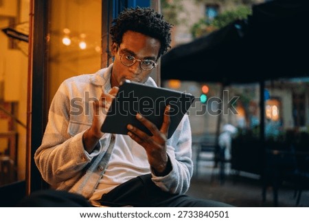 Focused young man using a digital tablet with a stylus, immersed in creative or technical work. This image conveys concentration and mobile productivity in a modern context.