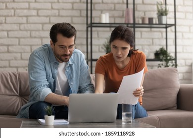 Focused young married couple looking at computer screen, involved in planning monthly household budget, holding paper bills making payments online in banking application, doing financial paperwork.