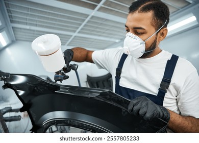 Focused young mechanic spray painting a car part while wearing protective gear and gloves - Powered by Shutterstock