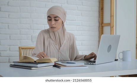 Focused young Muslim woman student in hijab dress studying hard, online education, university homework with laptop, books, notes