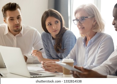 Focused Young Students Interns Workers Making Notes Listening To Old Senior Aged Female Manager Coach Mentor Leader Teacher Talking At Group Office Meeting Instructing Business Work Team With Laptop