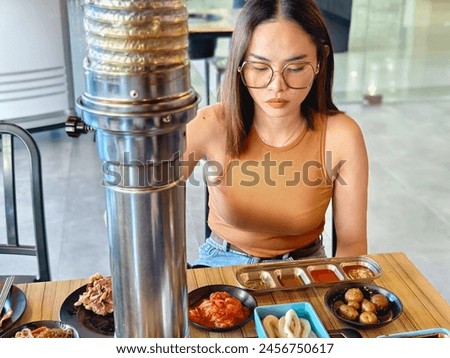 Focused young woman dining alone at a samgyupsal restaurant, surrounded by an assortment of traditional Korean side dishes.