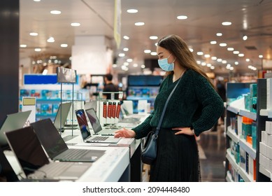 Focused Young Woman In Face Mask Examines Laptop On Display In Tech Store Department
