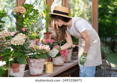 Focused young woman Gardener Tending to Flowers in Greenhouse in sunny day. small business owner - Powered by Shutterstock