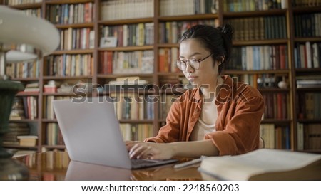 Focused young woman student spending time in university library, doing research, typing on laptop