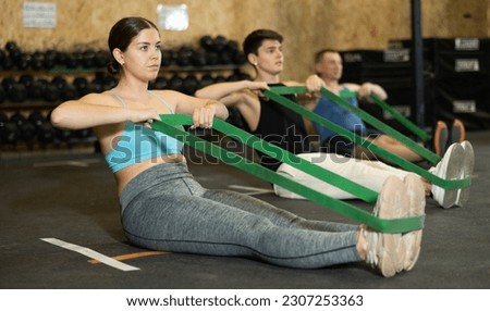 Focused young woman training with resistance band for health wellness, strong biceps or abs muscles in gym health center